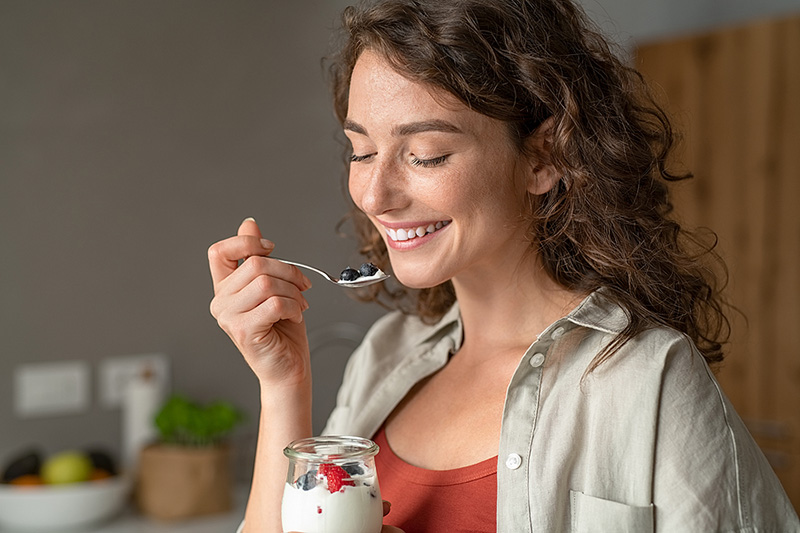 Smiling young woman eating yogurt.